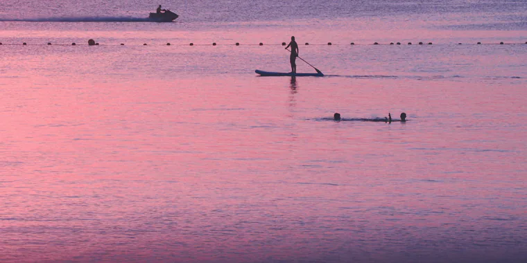 Iemand op een supboard op het roze, spiegelgladde water van de Mar Menor bij zonsondergang, bij La Manga