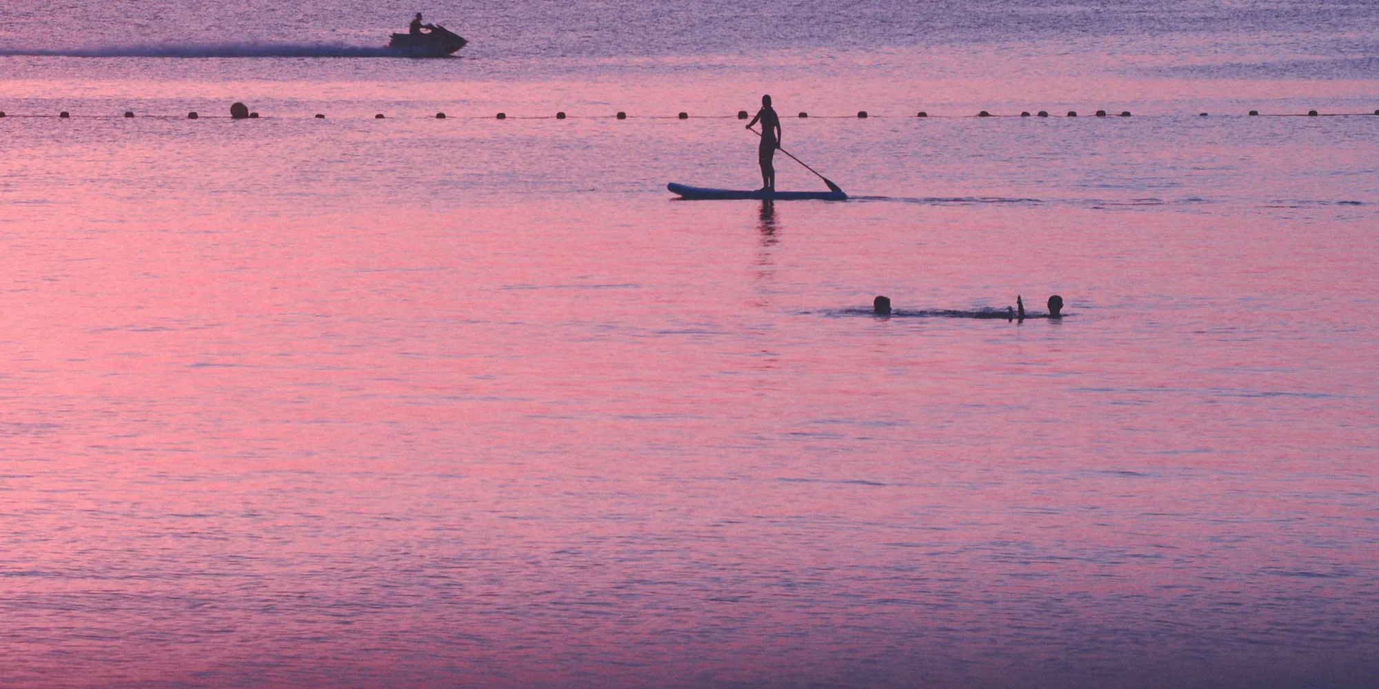 Una persona en tabla de paddle surf sobre el agua rosa y en calma del Mar Menor al atardecer, cerca de La Manga