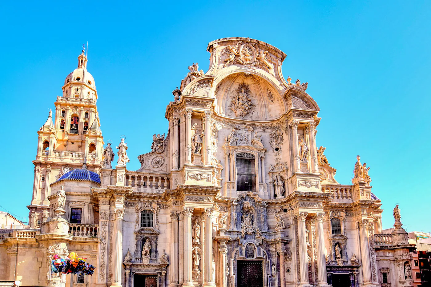 La fachada barroca llena de detalles de la catedral de Murcia bajo un cielo azul intenso
